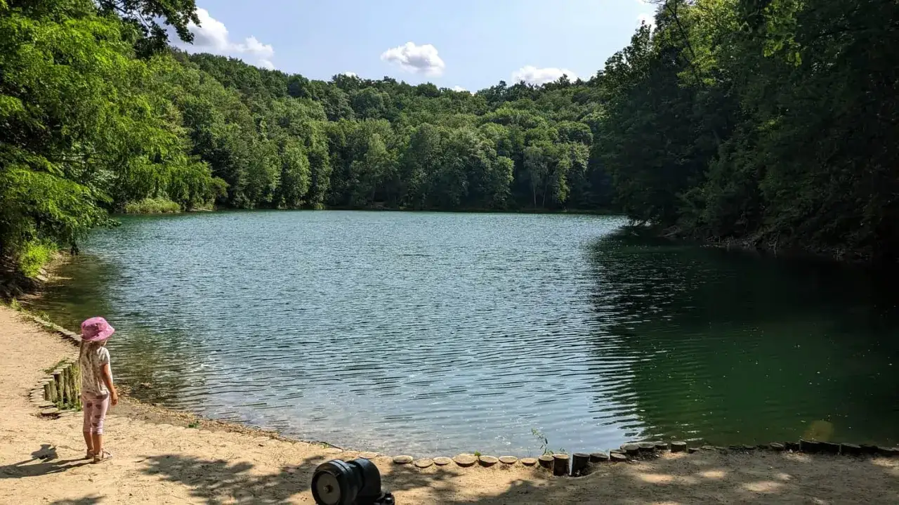 Dziewczynka w różowym kapeluszu podziwia spokojne jezioro otoczone lasem. Idealne miejsce na jednodniową wycieczkę, odkrywając **niemcy atrakcje niedaleko Szczecina**.