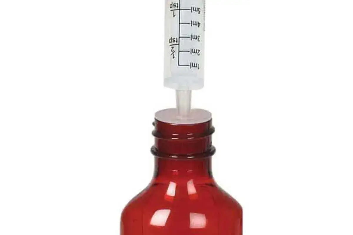 Spritze mit Markierungen f&uuml;r ml und Teel&ouml;ffel, die in eine rote Flasche eingef&uuml;hrt wird, um 1 ml abzumessen ohne messbecher.
