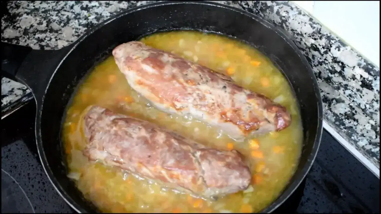 Dos solomillos de cerdo dorados se cocinan a fuego lento en una salsa con zanahorias picadas en una sart&eacute;n.