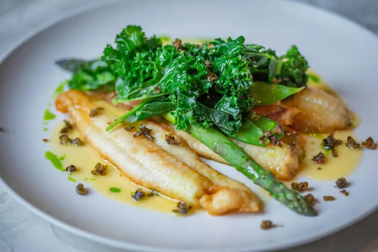 Filetes de pescado blanco con espárragos, kale y guisantes, bañados en una ligera salsa verde.