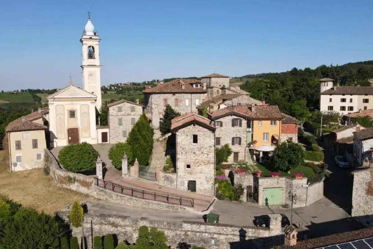 Un pittoresco borgo medievale vicino Pavia, con una chiesa imponente e case in pietra arroccate su una collina verdeggiante.