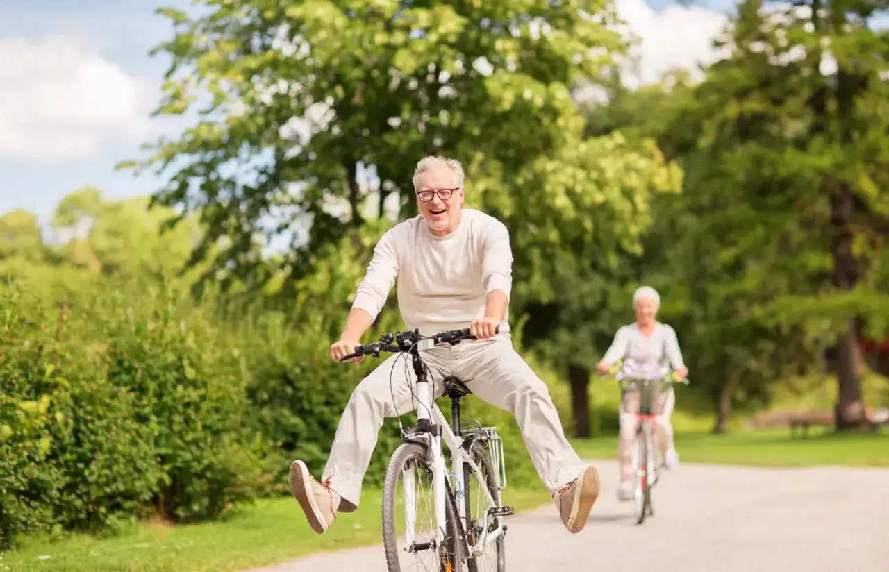 Ein Mann im engagierten Ruhestand lacht und f&auml;hrt ausgelassen Fahrrad, w&auml;hrend im Hintergrund eine Frau auf ihrem Rad f&auml;hrt.