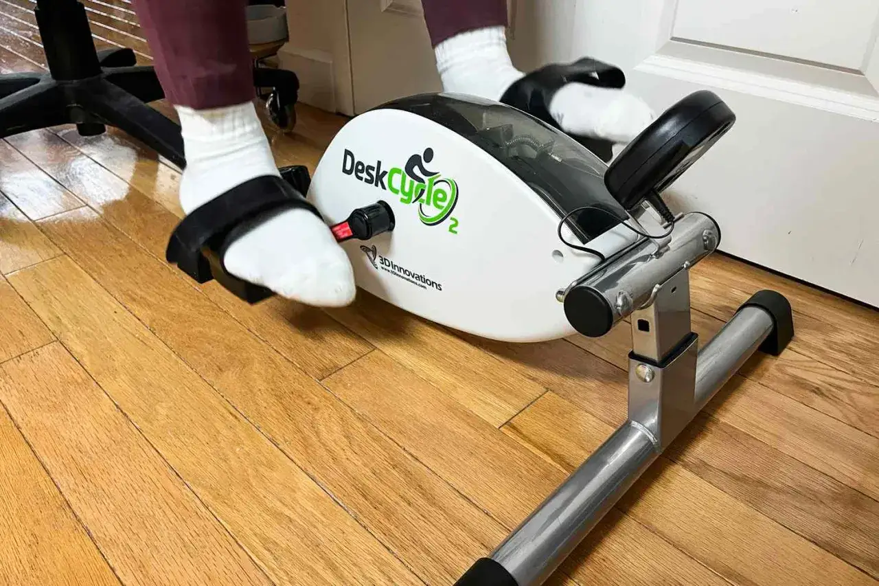 A person uses a pedal exerciser, a compact alternative to a stationary bike, for a low-impact workout while seated.