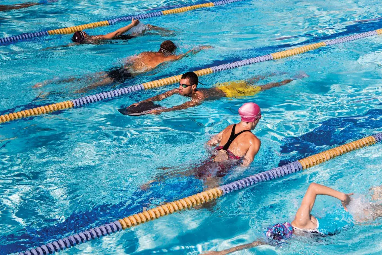 Several lap swimmers train in a pool, with one using a kickboard.