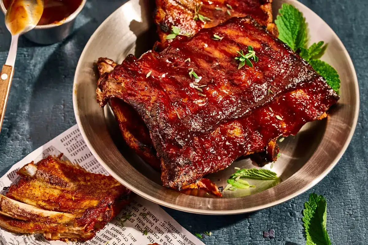 Saftige Spareribs sous vide, glasiert mit BBQ-Sauce und garniert mit Kräutern und Minze.