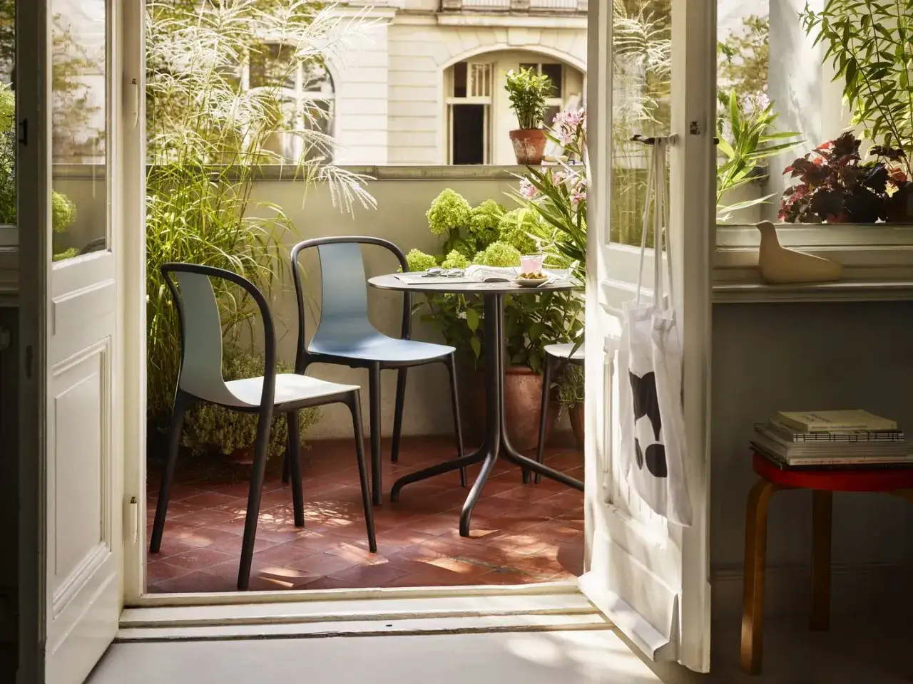 Un angolo relax con sedie moderne e un tavolino, circondato da piante rigogliose. Un esempio di come arredare balconi con stile e funzionalità.