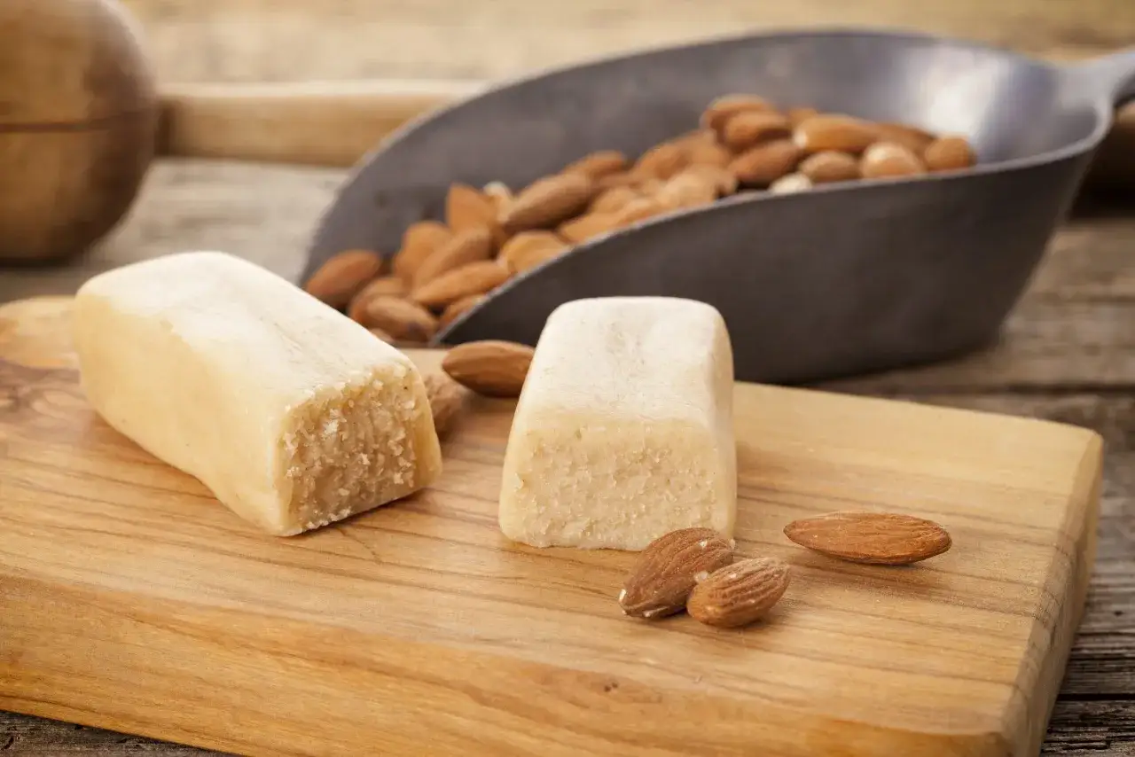 Deux blocs de p&acirc;te d'amande et des amandes enti&egrave;res sur une planche en bois. Id&eacute;al pour une recette p&acirc;te d'amande maison.