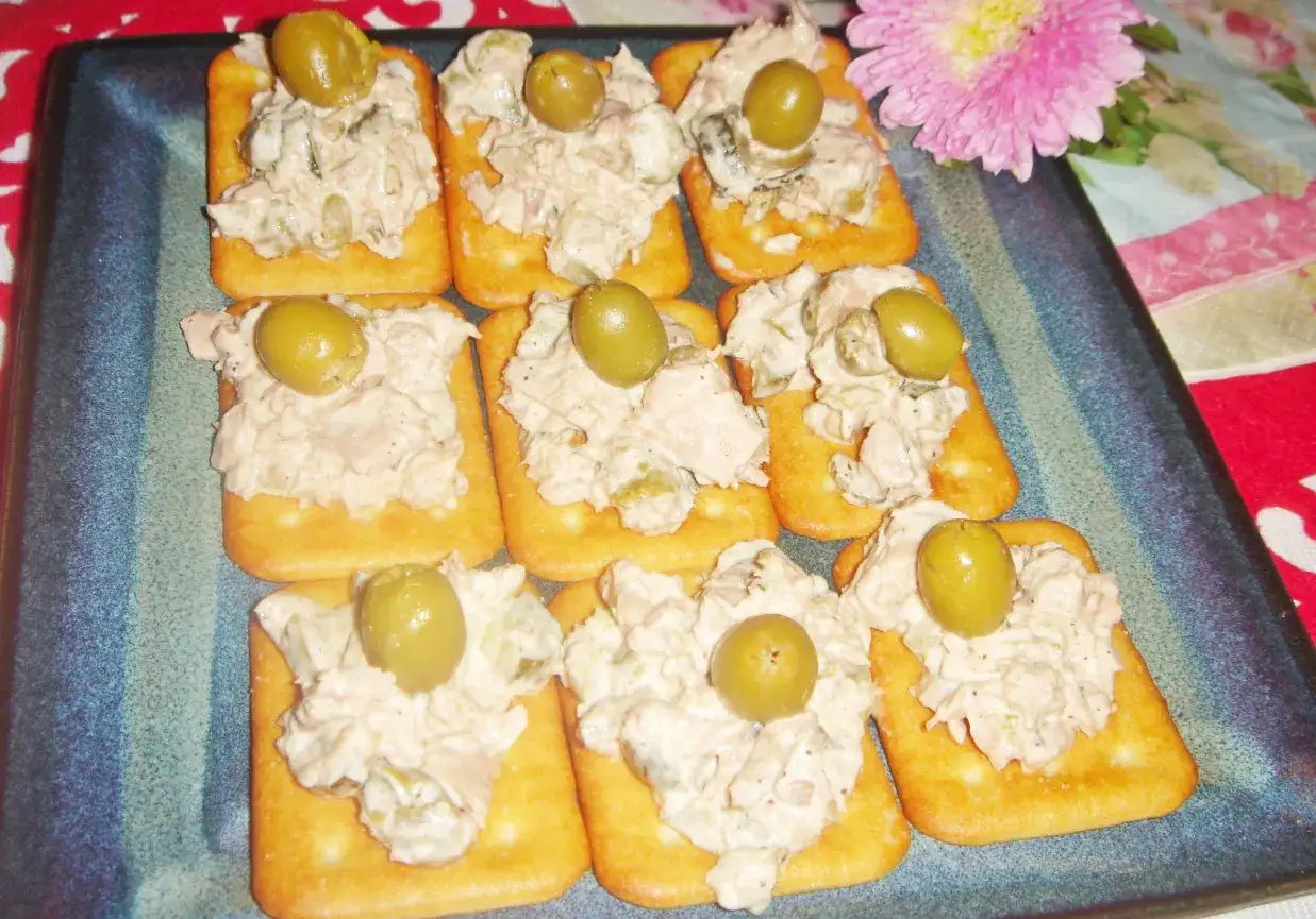 Pyszna pasta z tuńczyka na krakersach, ozdobiona oliwkami. Idealna przekąska na imprezę.
