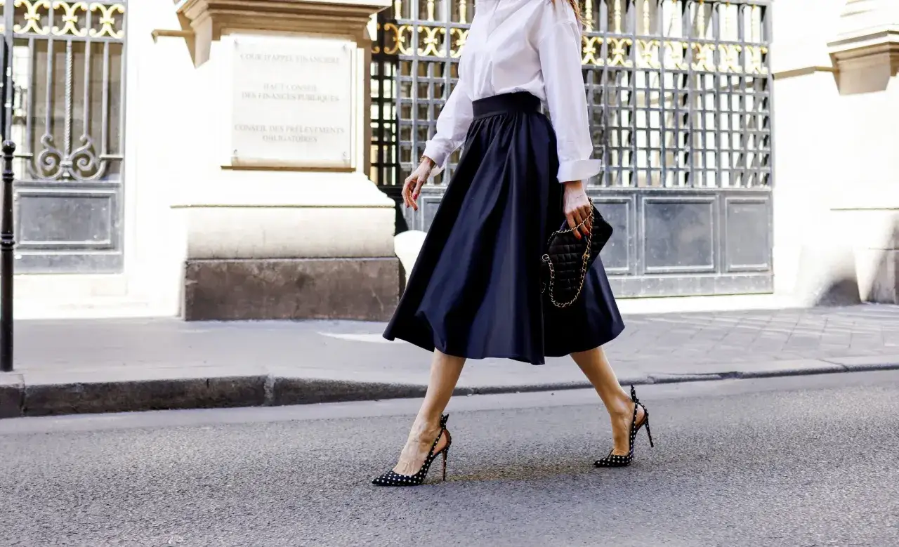 Elegante mujer pasea con su falda midi azul marino, camisa blanca y zapatos de lunares.
