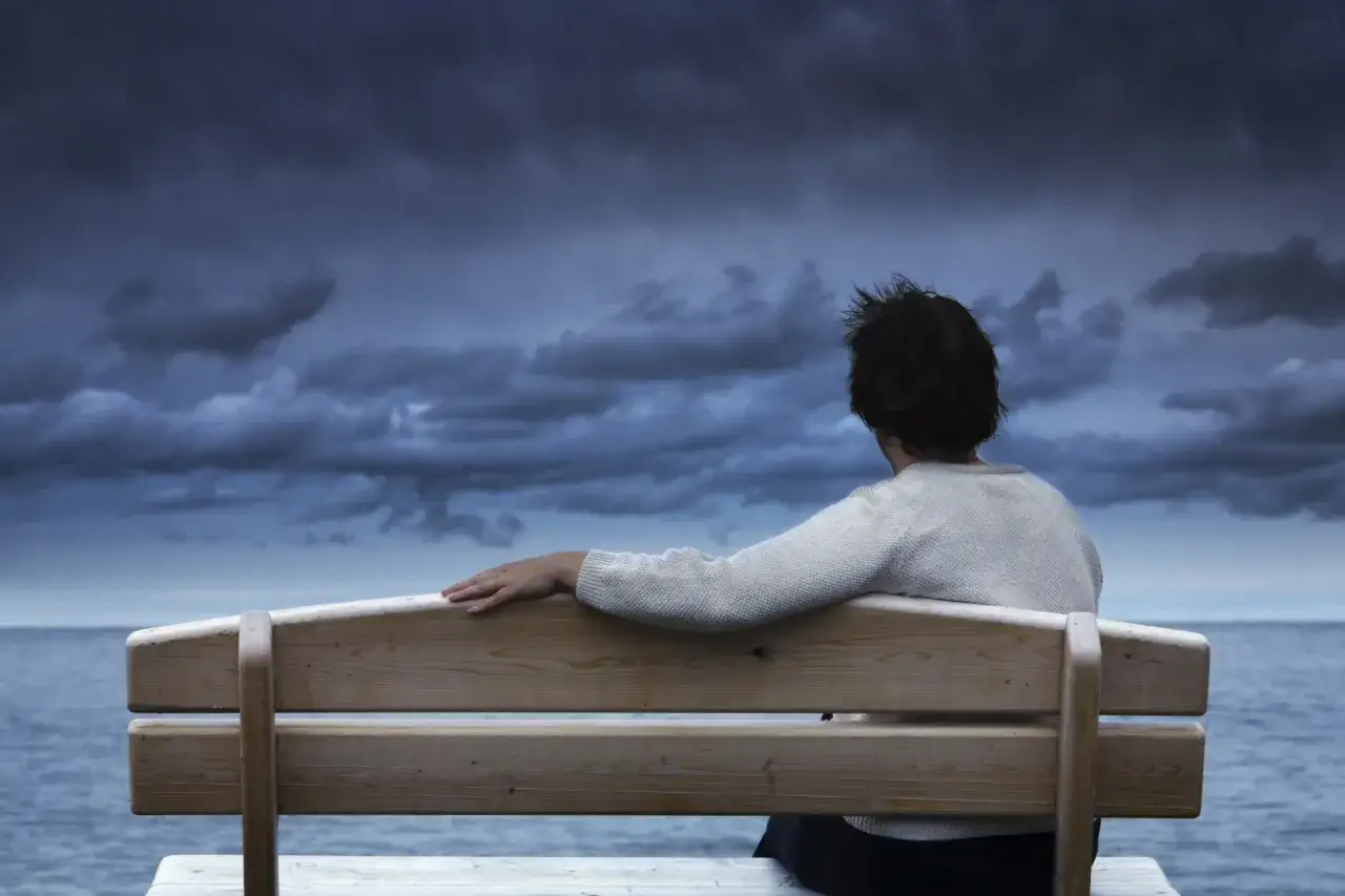 Persona seduta su una panchina guarda il mare tempestoso, un momento di riflessione per lasciare andare un uomo.