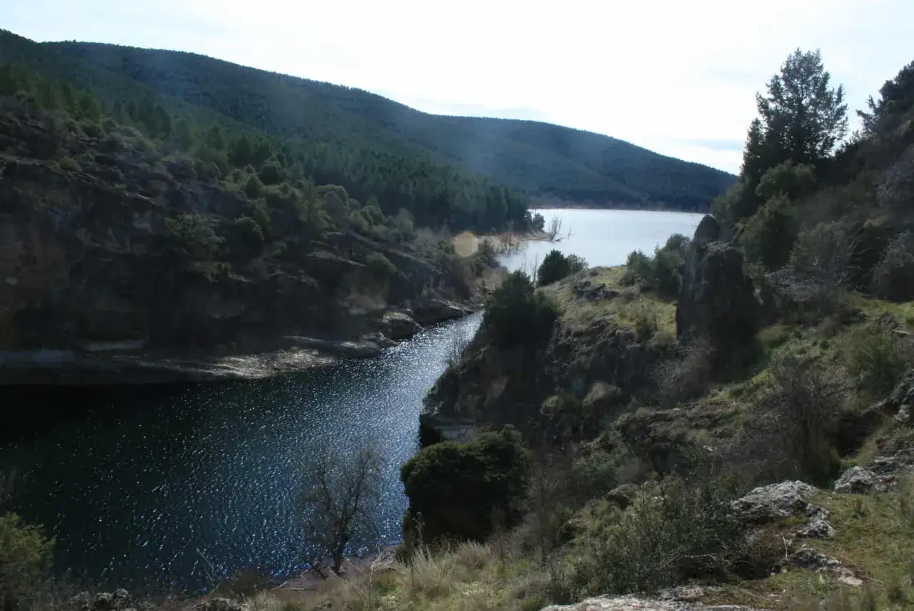 Paisaje natural con el **r&iacute;o Bornova** serpenteando entre colinas boscosas y rocosas. El agua refleja el cielo nublado.