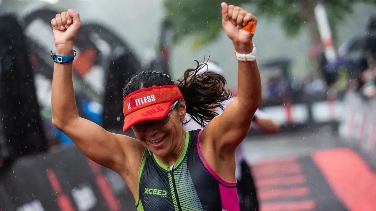 Jubelnde Athletin nach dem Ironman-Rennen, die die hohen Anforderungen gemeistert hat. Regen fällt, sie ist erschöpft, aber glücklich.