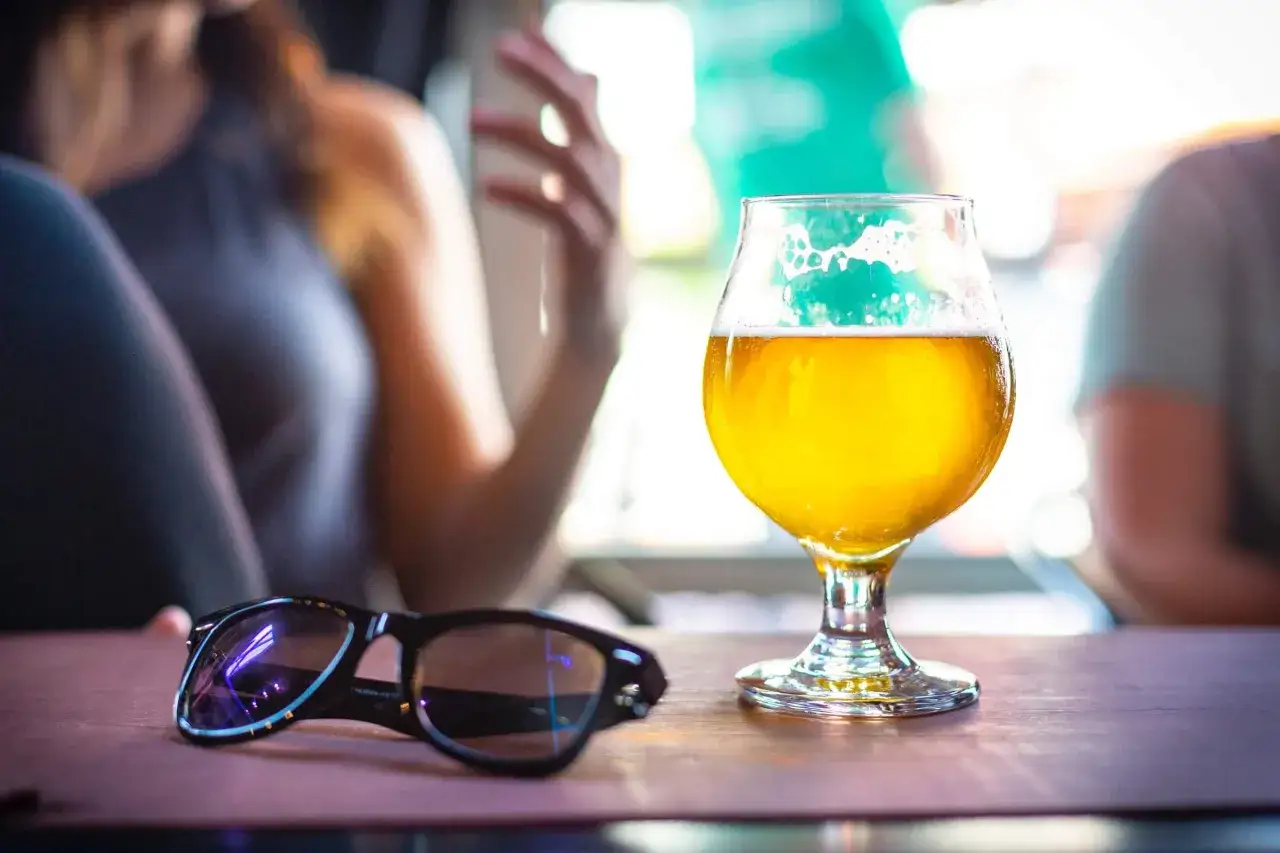 Un verre de bière de printemps doré, mousseux, sur une table en bois, avec des lunettes de soleil à côté.