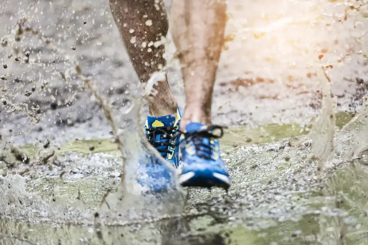 Des chaussures trail hiver bleues traversent une flaque de boue, projetant des éclaboussures.