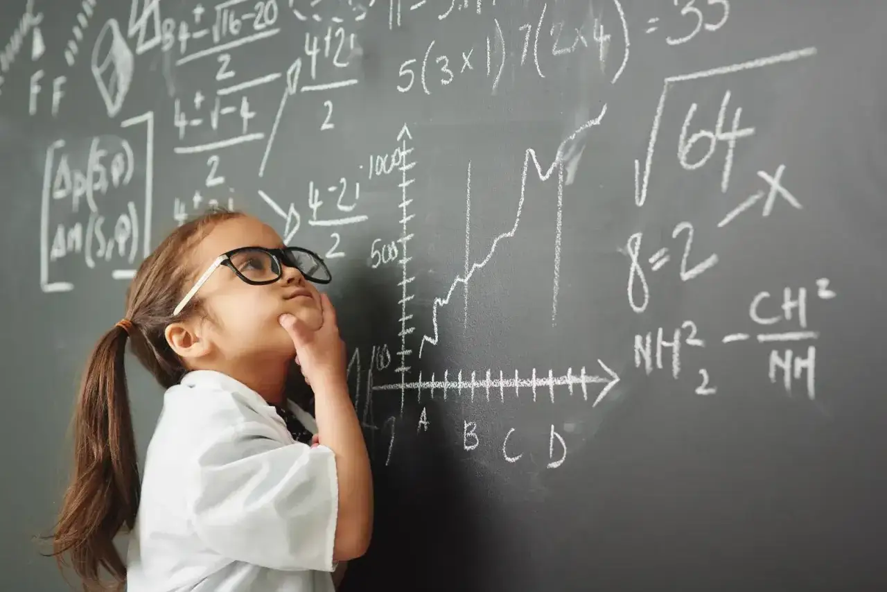 Dziewczynka w okularach zamyślona przy tablicy pełnej równań. Nawet z dyskalkulią można próbować zrozumieć matematykę.