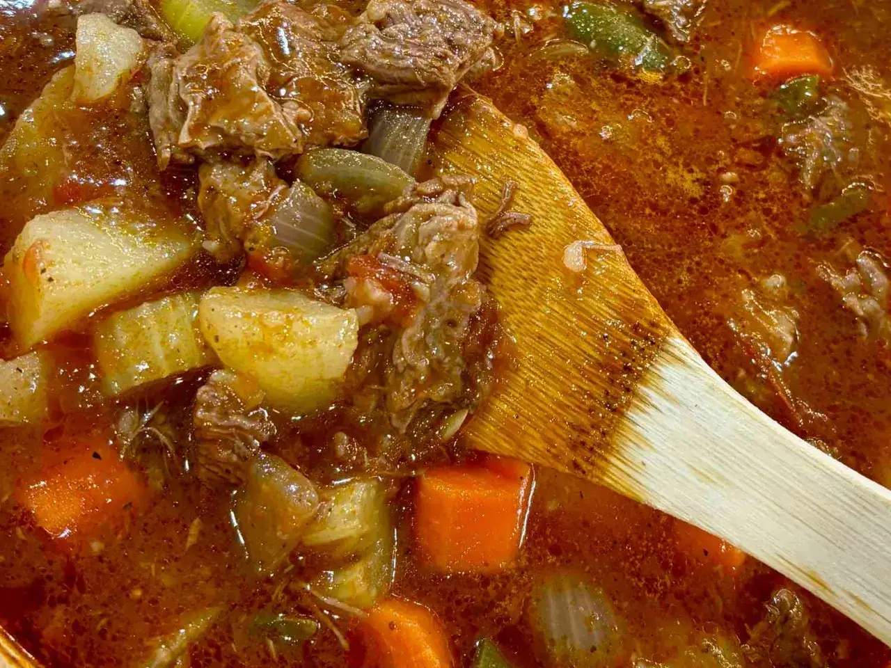 Un plat mijot&eacute; r&eacute;confortant : quelle viande avec sauce tomate, pommes de terre et carottes, m&eacute;lang&eacute; avec une cuill&egrave;re en bois.