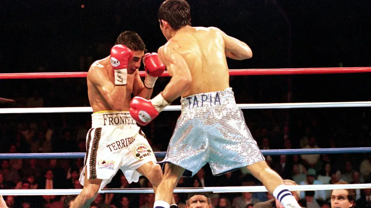 Marco Antonio boxer in action, throwing a punch in a boxing ring. His opponent, Tapia, defends.