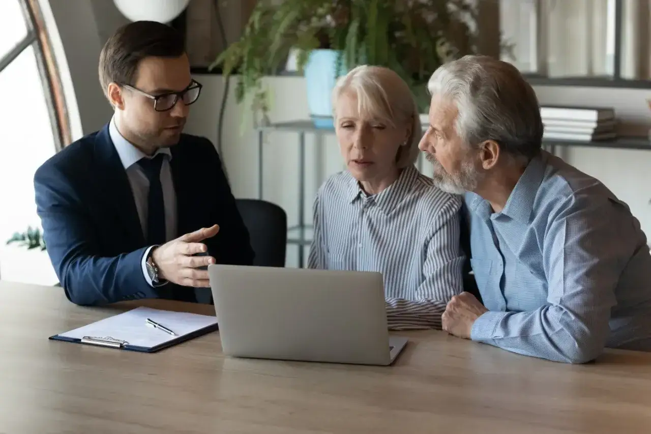 Prawnik omawia z parą starszych ludzi automatyczne przyjęcie spadku, wskazując na ekran laptopa.