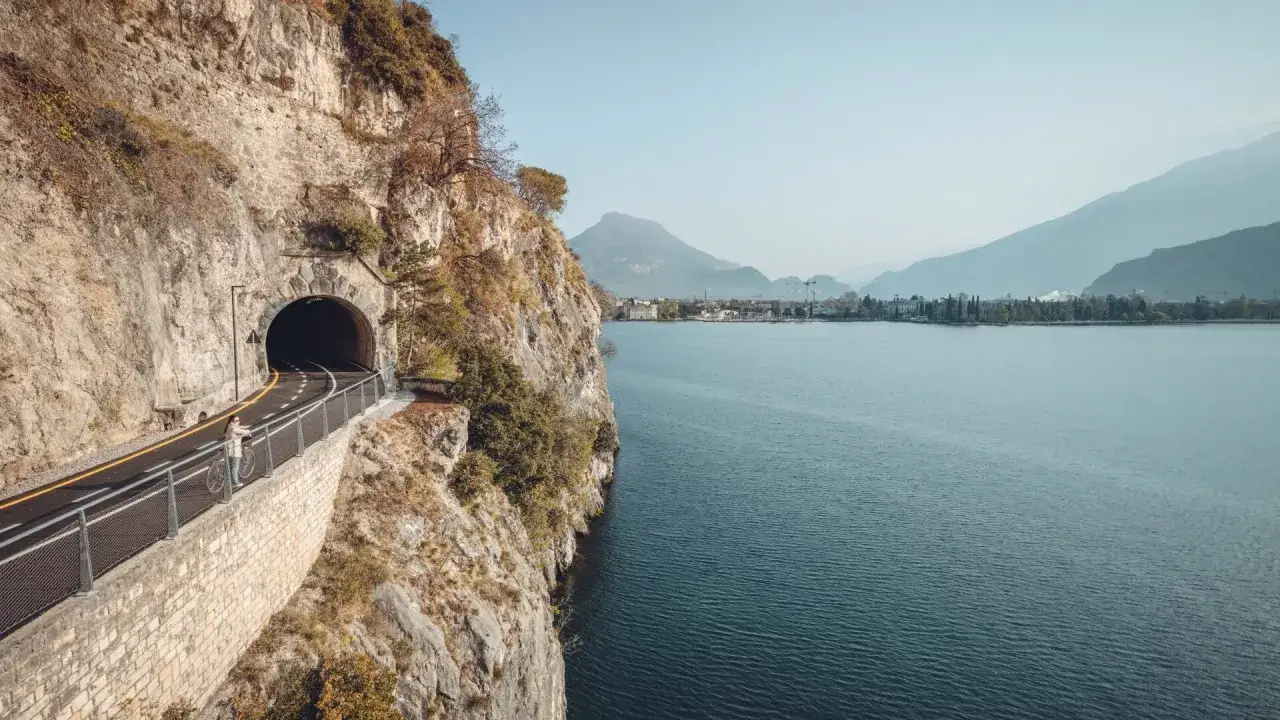 Ciclabile Riva del Garda: una ciclista ammira il lago e il tunnel scavato nella roccia.