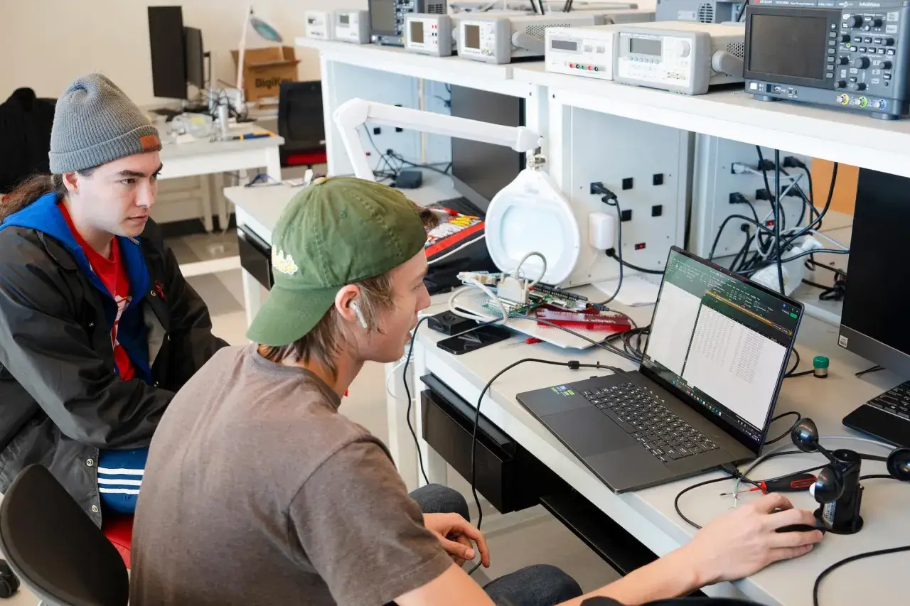 Dwóch studentów pracuje nad projektem, analizując dane na laptopie w pracowni.