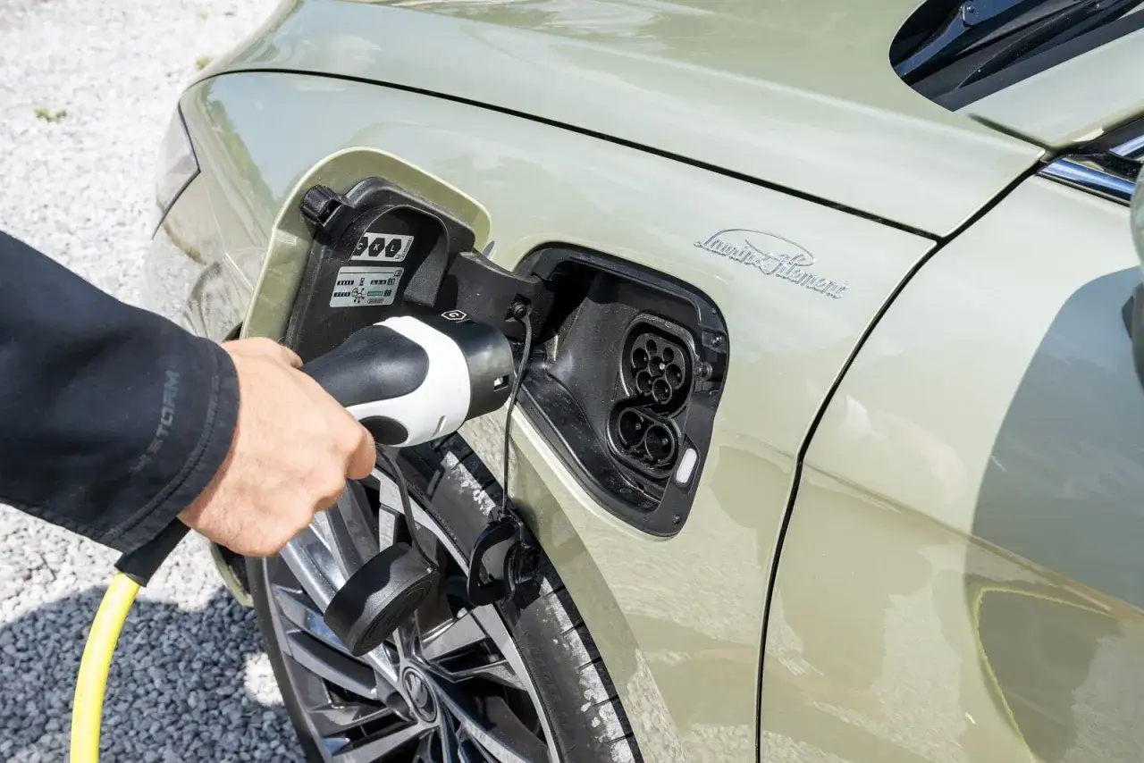 Ręka podłącza superb plug in do gniazda ładowania samochodu elektrycznego.