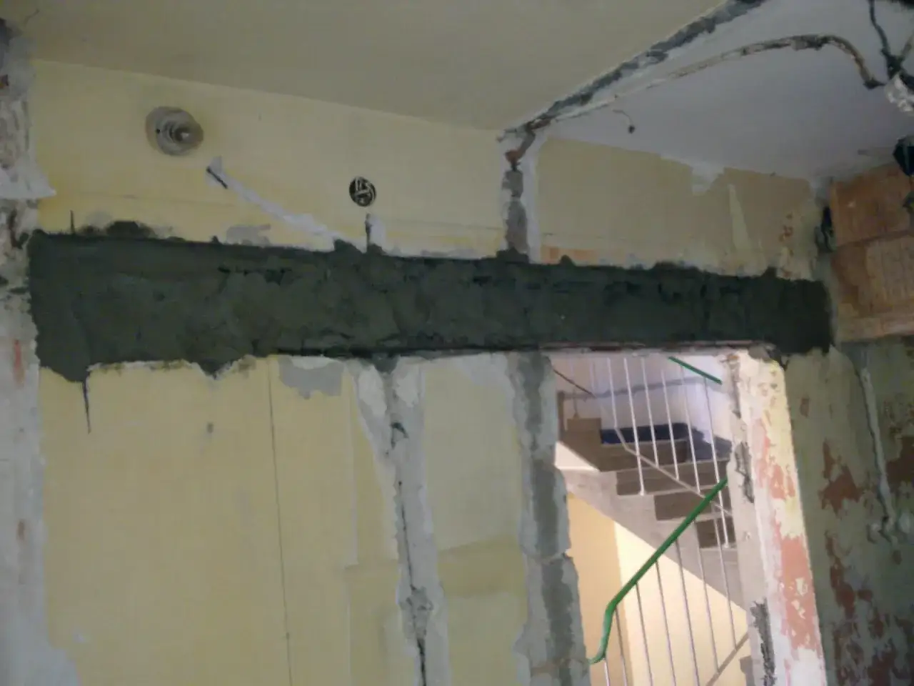 Częściowe wyburzenie ściany nośnej z widocznym nowym nadprożem z betonu. W tle schody.