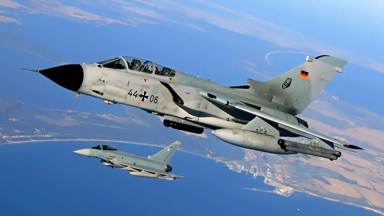 Zwei deutsche Kampfflugzeuge, ein PA-200 Tornado und ein Eurofighter, fliegen &uuml;ber K&uuml;stenlandschaft.