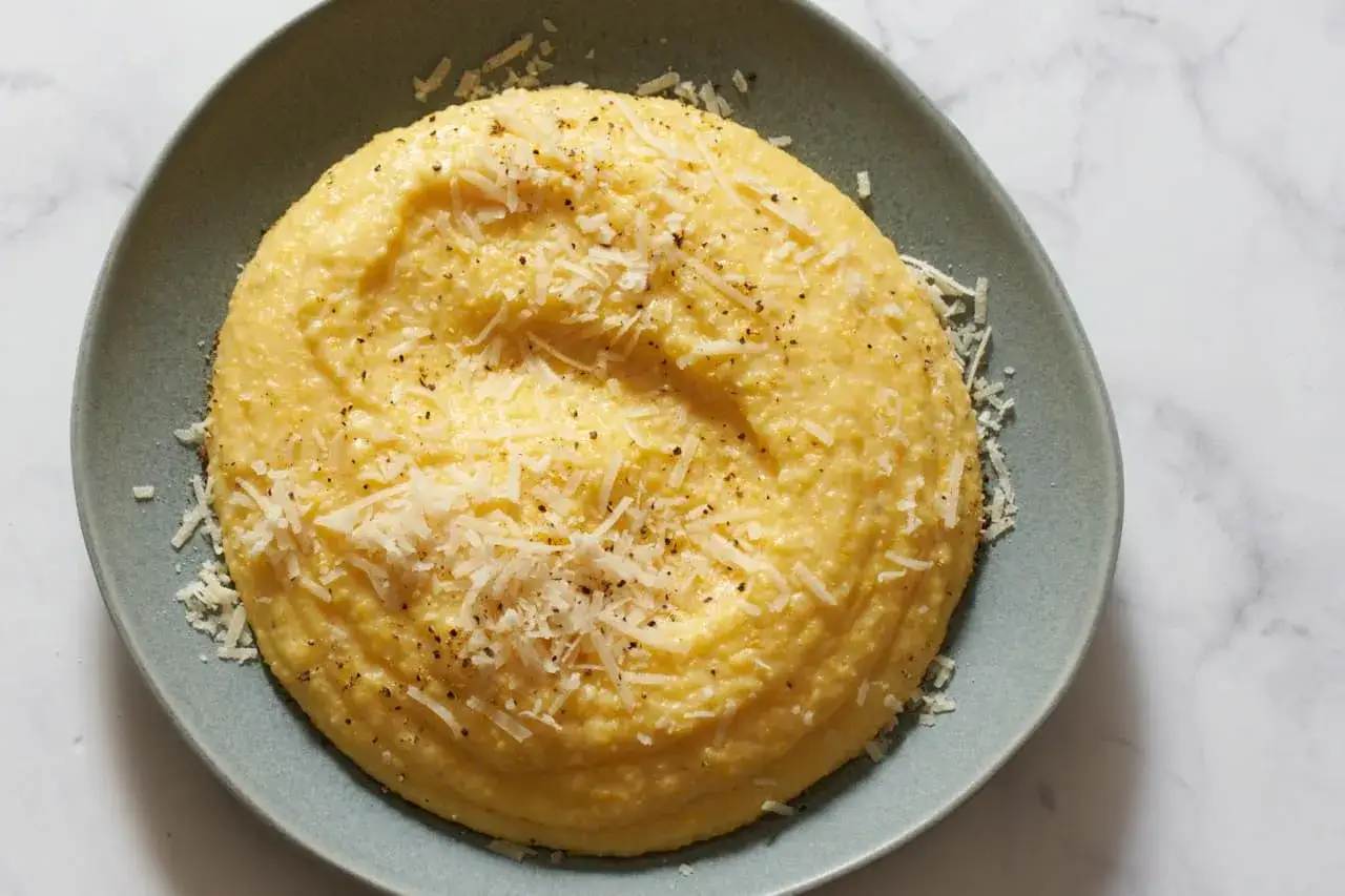 Un plato de polenta cremosa, espolvoreada con queso rallado y pimienta negra.