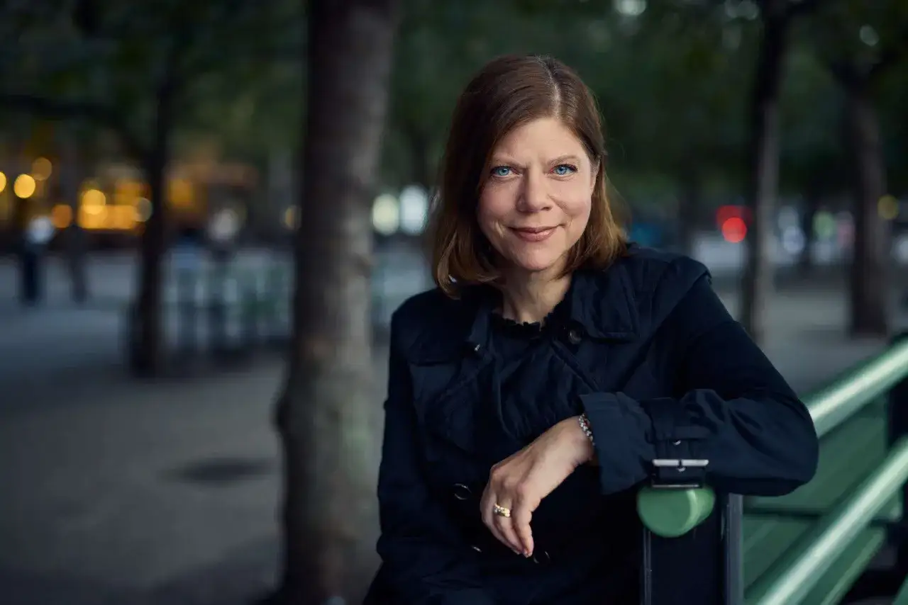 Charlotte al-Khalili sitter på en parkbänk i skymningen, klädd i en mörk rock.