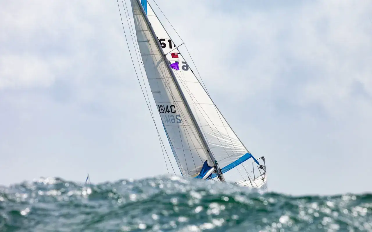 Vela bianca gonfiata dal vento, con numeri neri e bandierine, solca le onde. La velocit&agrave; della barca a vela &egrave; palpabile.