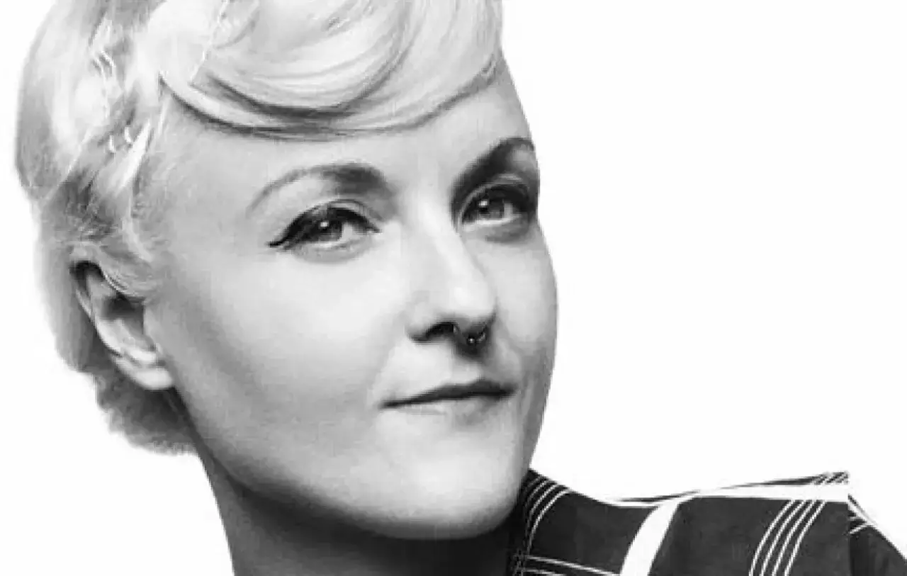 Porträtt av en kvinna med en klassisk bea szenfeld frisyr, markerad eyeliner och en näspiercing.