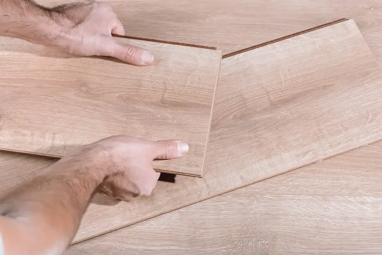 Manos separando tablas de suelo laminado de madera clara.