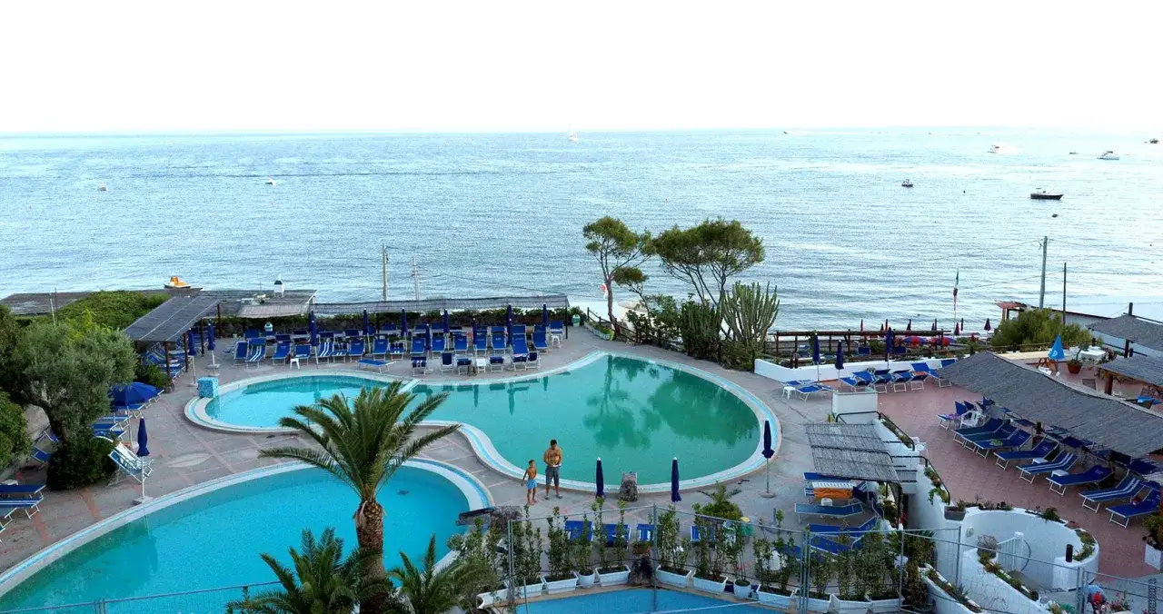 Piscine e lettini a **Maronti Ischia**, con il mare azzurro sullo sfondo e qualche barca all'orizzonte.