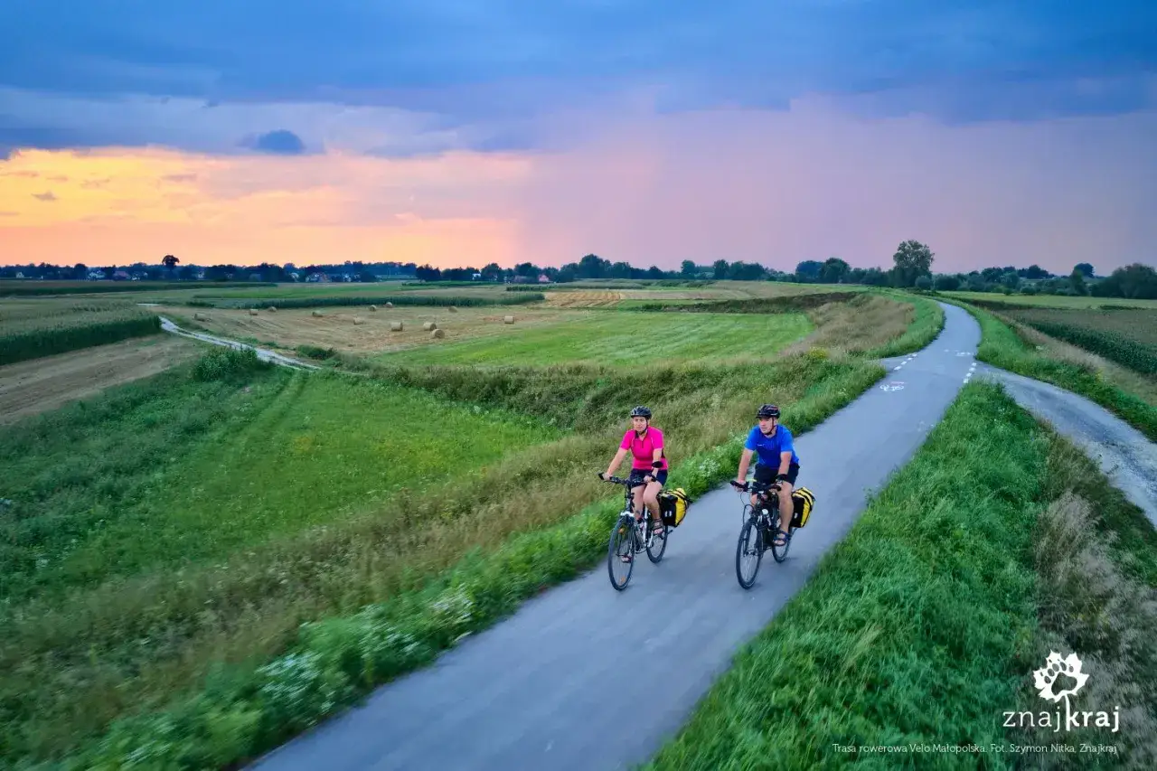 Para na rowerach przemierza malownicze trasy rowerowe Tarn&oacute;w. Zach&oacute;d słońca nad polami tworzy piękne tło dla ich podr&oacute;ży.
