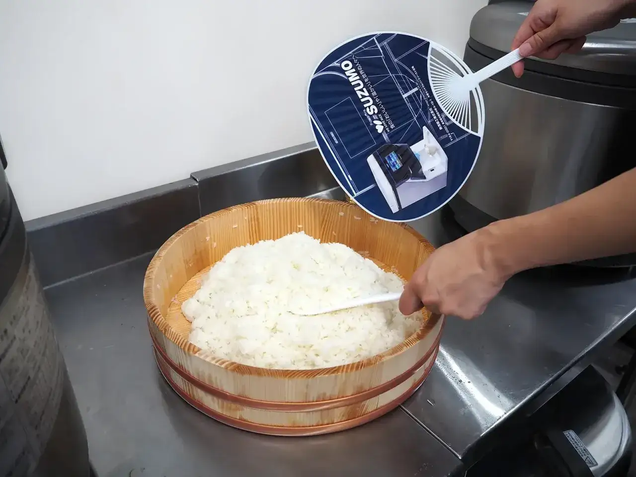 F&auml;rskt sushiris i en tr&auml;sk&aring;l, redo f&ouml;r ditt sushiris recept. En hand fl&auml;ktar riset med en bl&aring; fl&auml;kt.