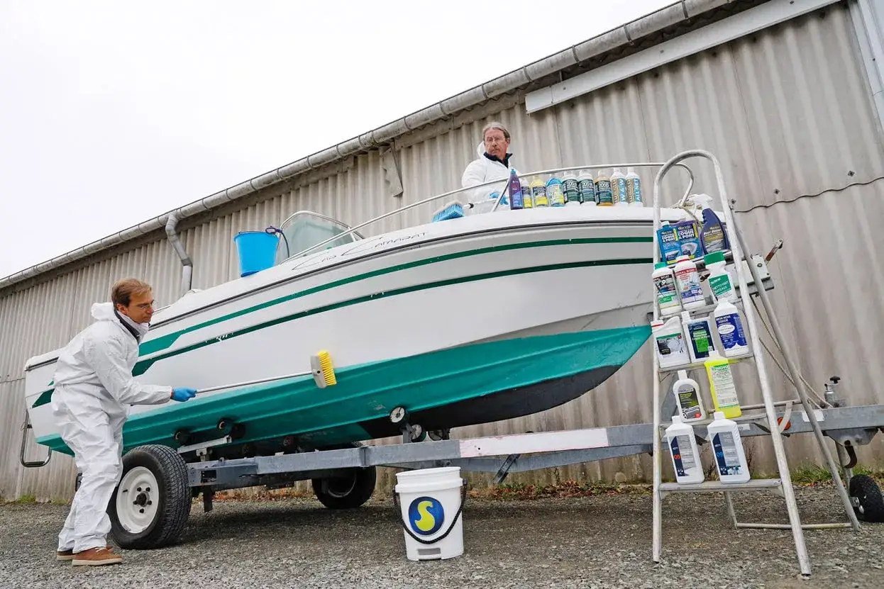 Un homme en combinaison blanche nettoie un bateau hors de l'eau, pr&ecirc;t pour l'entretien.