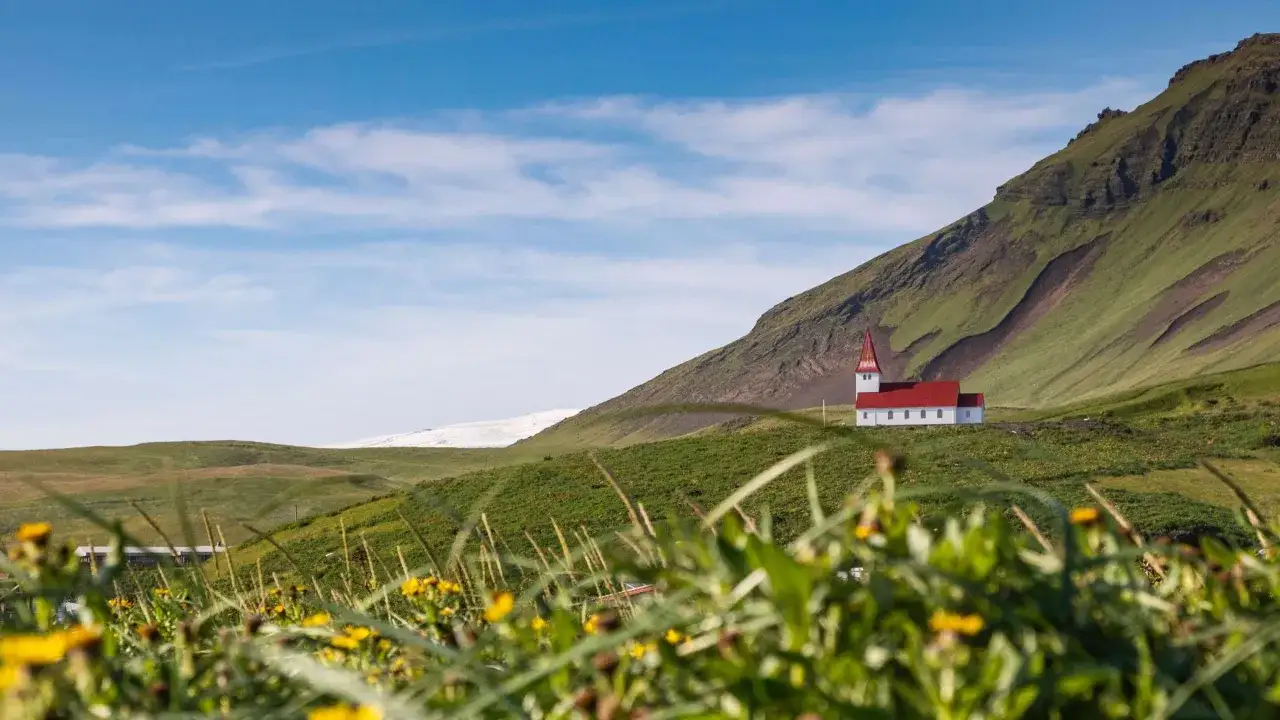 Letnia Islandia: malowniczy biały kościółek z czerwoną wieżą na tle zielonych wzgórz i lodowca. Idealne miejsce na wakacje!