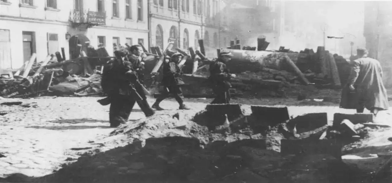Zniszczone ulice Warszawy, powstańcy idący przez gruzy. Czy powstanie warszawskie miało sens? Trudne pytanie w obliczu tej tragedii.