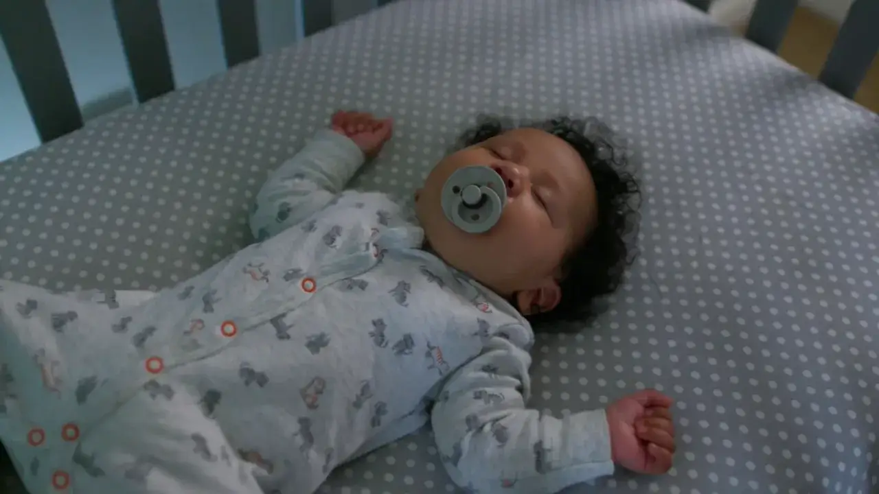 Un beb&eacute; de 3 meses con chupete duerme pl&aacute;cidamente en su cuna. A pesar de las noches en vela, este peque&ntilde;o finalmente descansa.