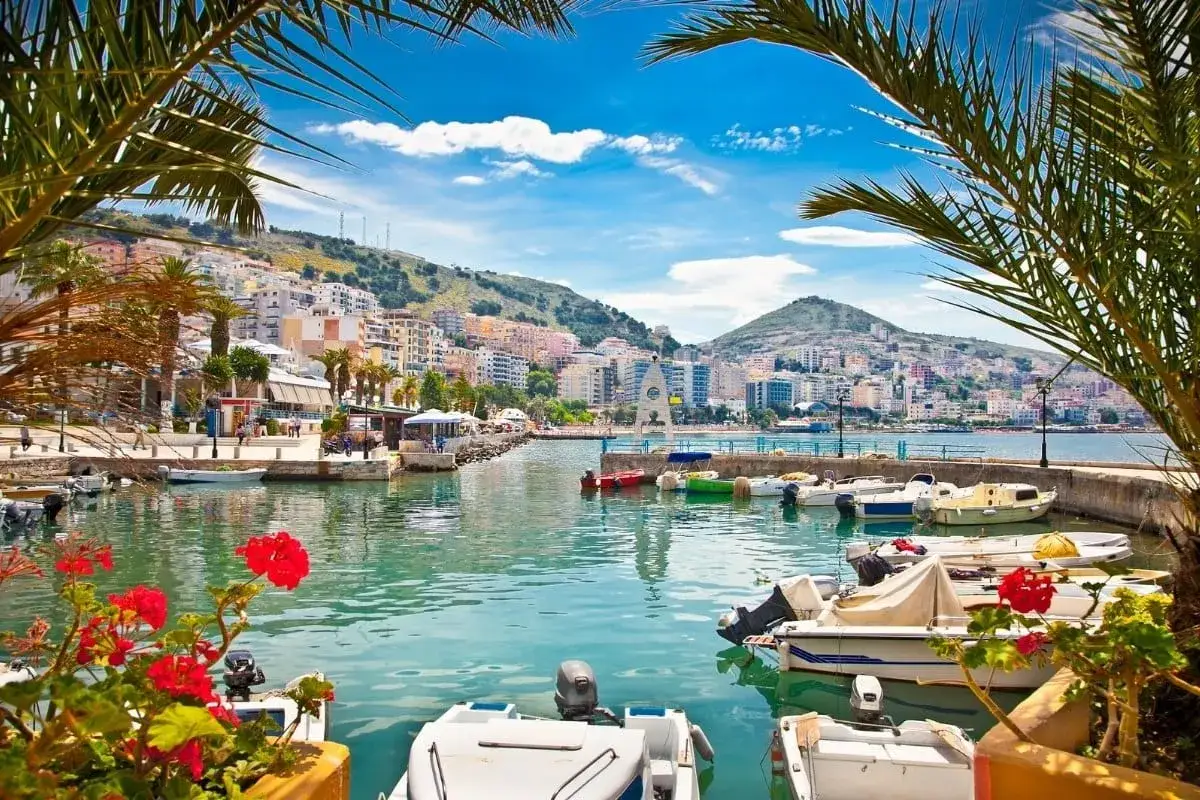 Malowniczy port w jednym z albania miasta turystyczne. Woda lśni, łodzie kołyszą się, a w tle widać kolorowe budynki na wzg&oacute;rzu.