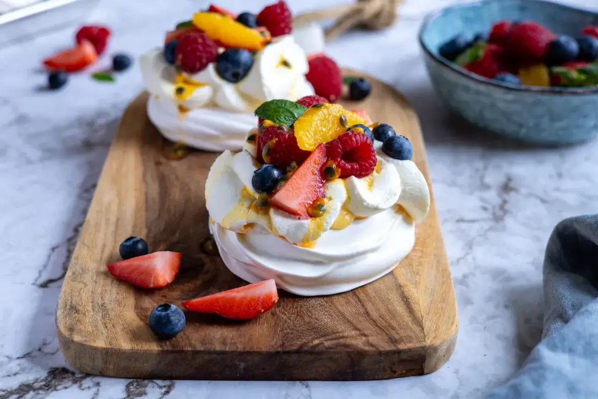 Två läckra pavlova tårtor toppade med grädde och färska bär som jordgubbar, blåbär, hallon och passionsfrukt.