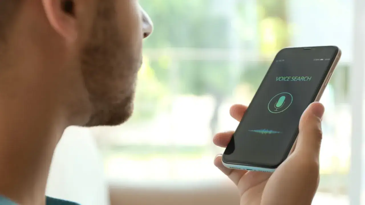 Mężczyzna używa telefonu do wyszukiwania głosowego. Na ekranie widnieje ikona mikrofonu i napis