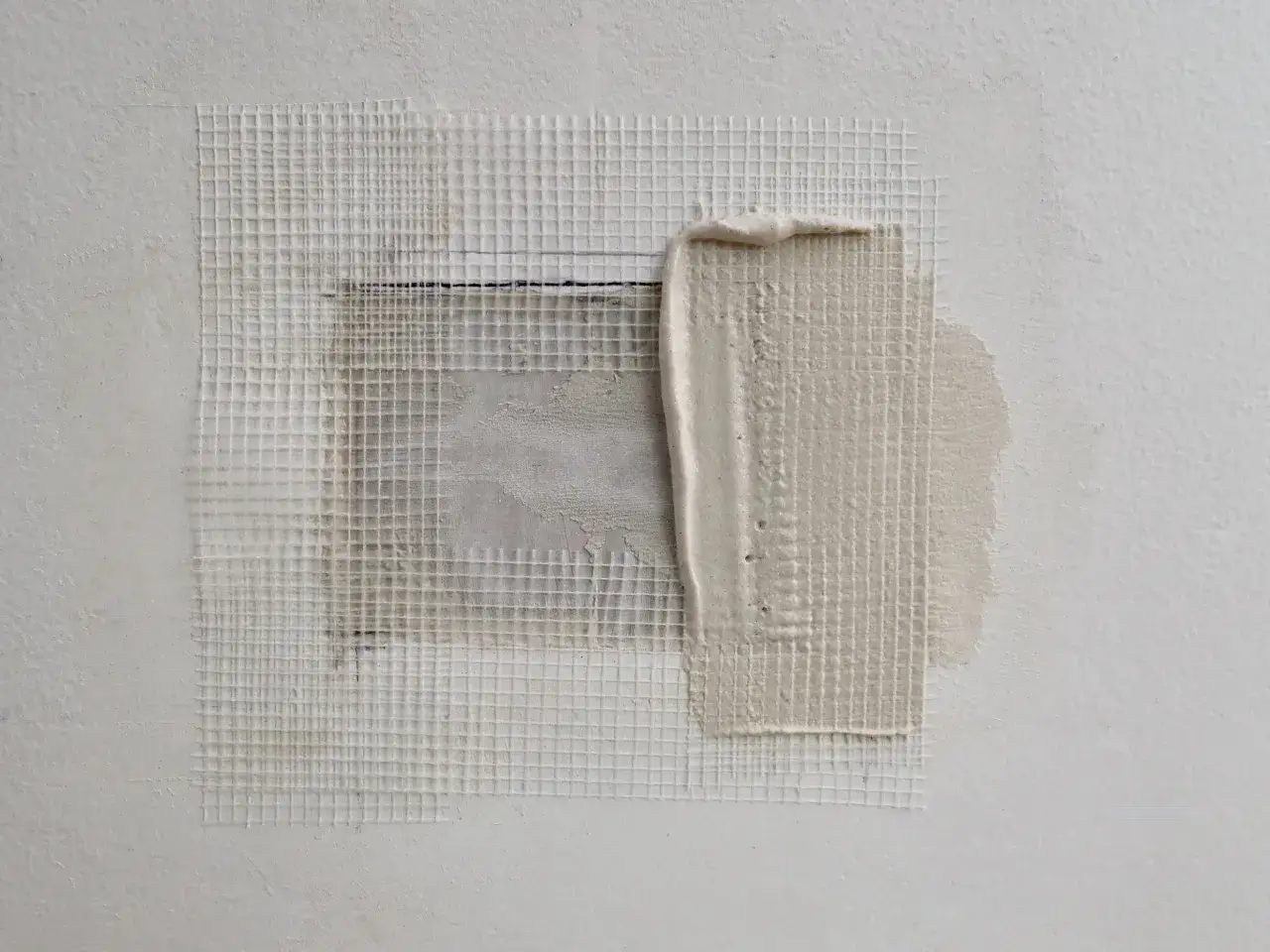 Riparazione di un buco nel muro troppo grande con rete e stucco. La rete a maglie quadrate copre l'area danneggiata, pronta per essere livellata.