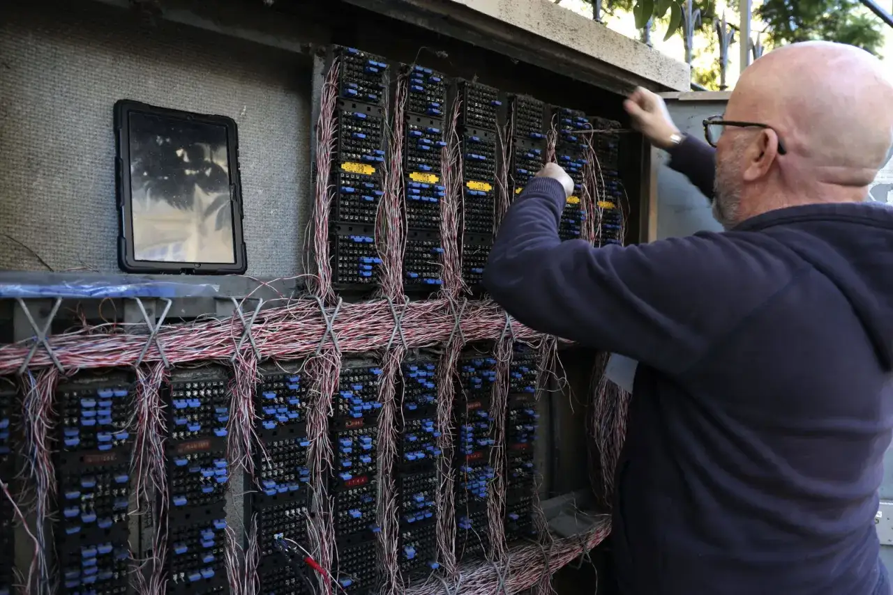 Un technicien ajuste les câbles d'un répartiteur téléphonique, peut-être pour une connexion ADSL Bouygues. Une tablette est posée à côté.