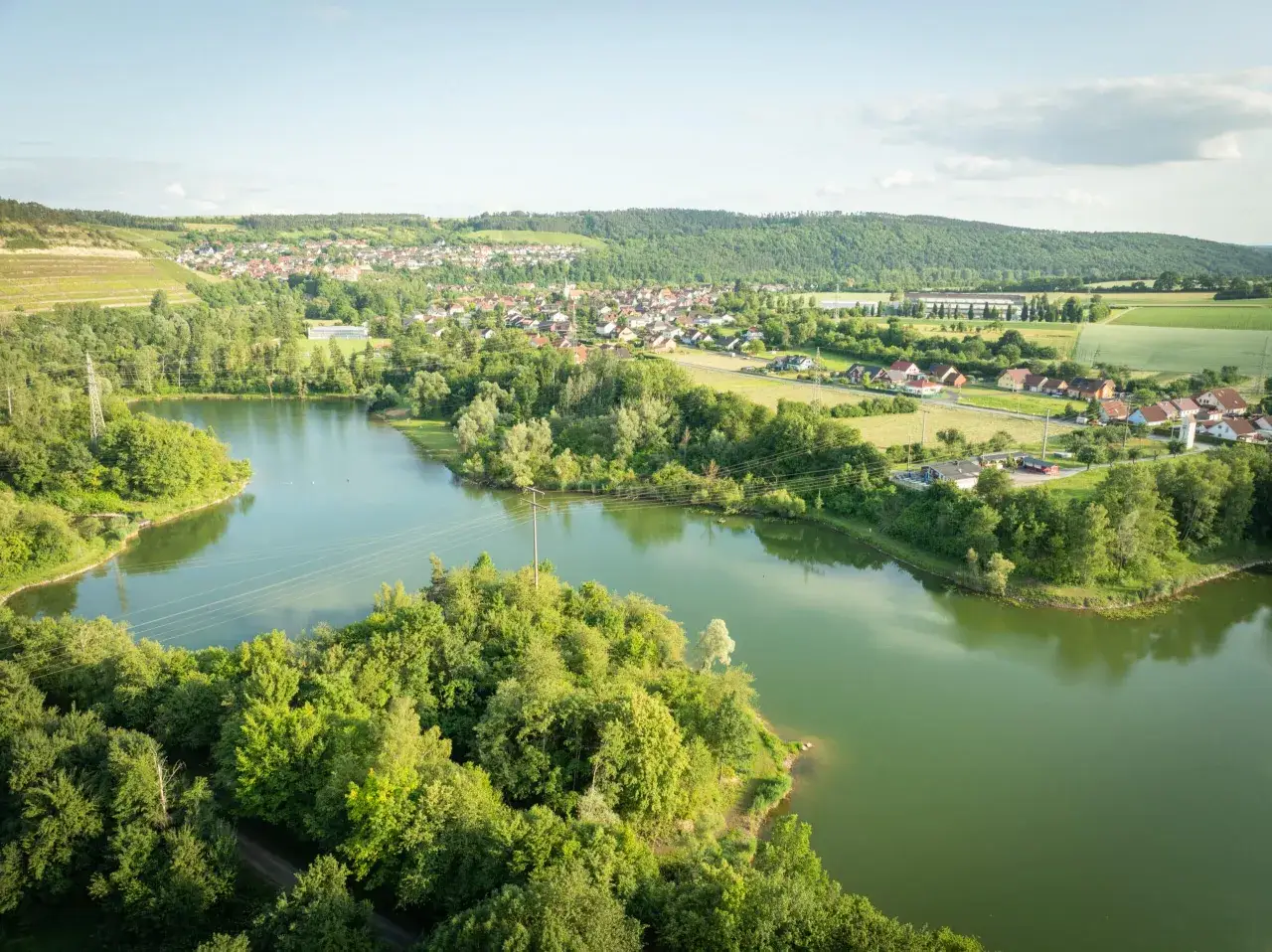 Gr&uuml;ne H&uuml;gel, ein Dorf und der glitzernde Klostersee Triefenstein im Sommer.
