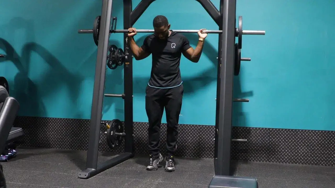 Mann im Fitnessstudio mit Langhantel f&uuml;r Calf Raises.