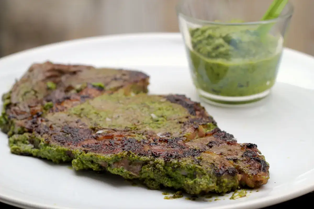Entrecôte grillée, généreusement recouverte d'un assaisonnement vert vif, servie avec une sauce d'accompagnement.