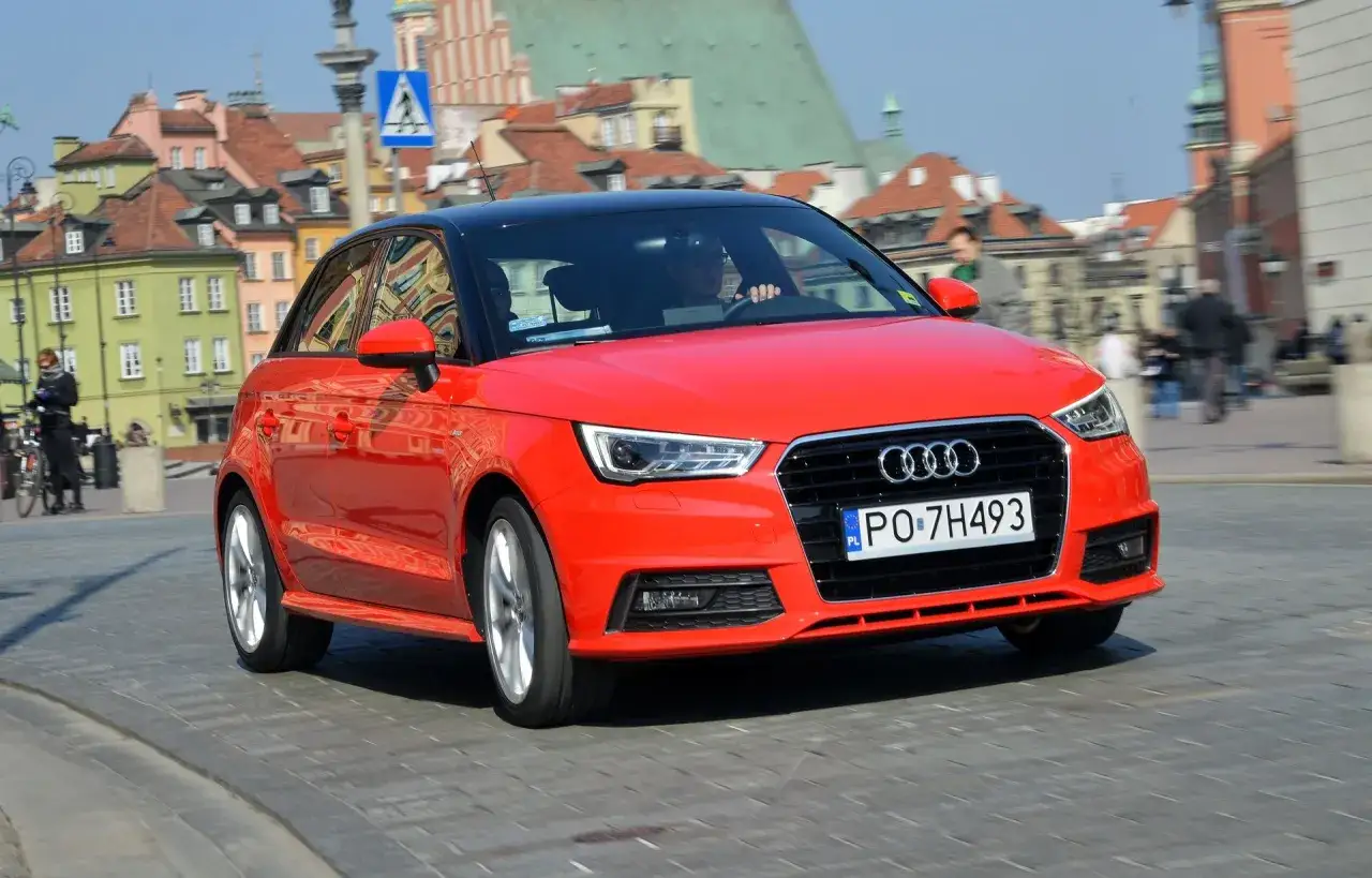 Czerwone audi 1 z czarnym dachem jedzie po brukowanej ulicy w historycznym mieście.