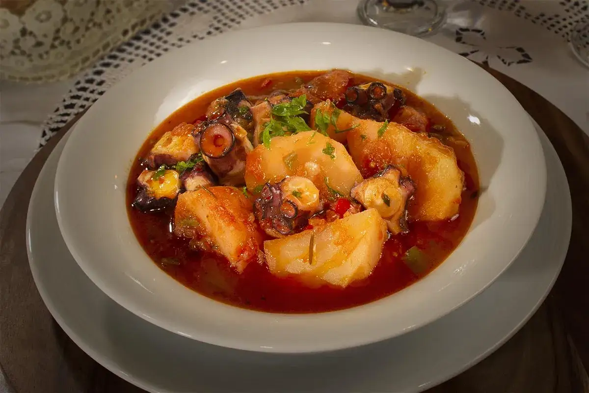 Un delicioso pulpo a la mugardesa, con patatas tiernas y una salsa roja sabrosa, servido en un plato blanco.