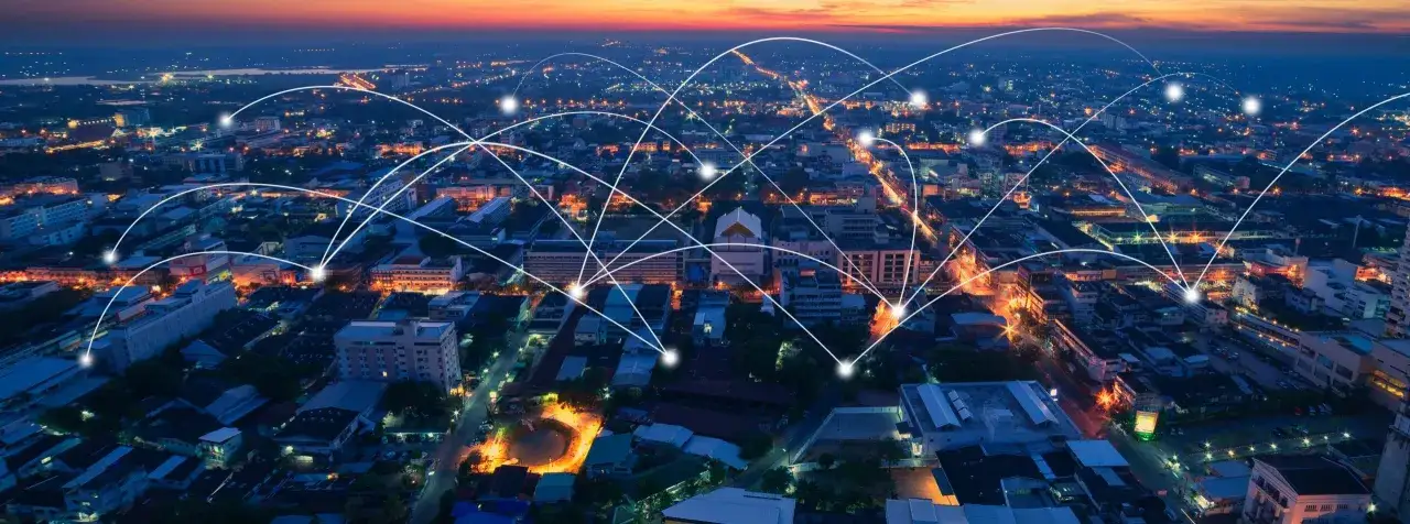 A city at dusk, illuminated by streetlights and building lights, with a network of glowing lines connecting various points, symbolizing network infrastructure services.